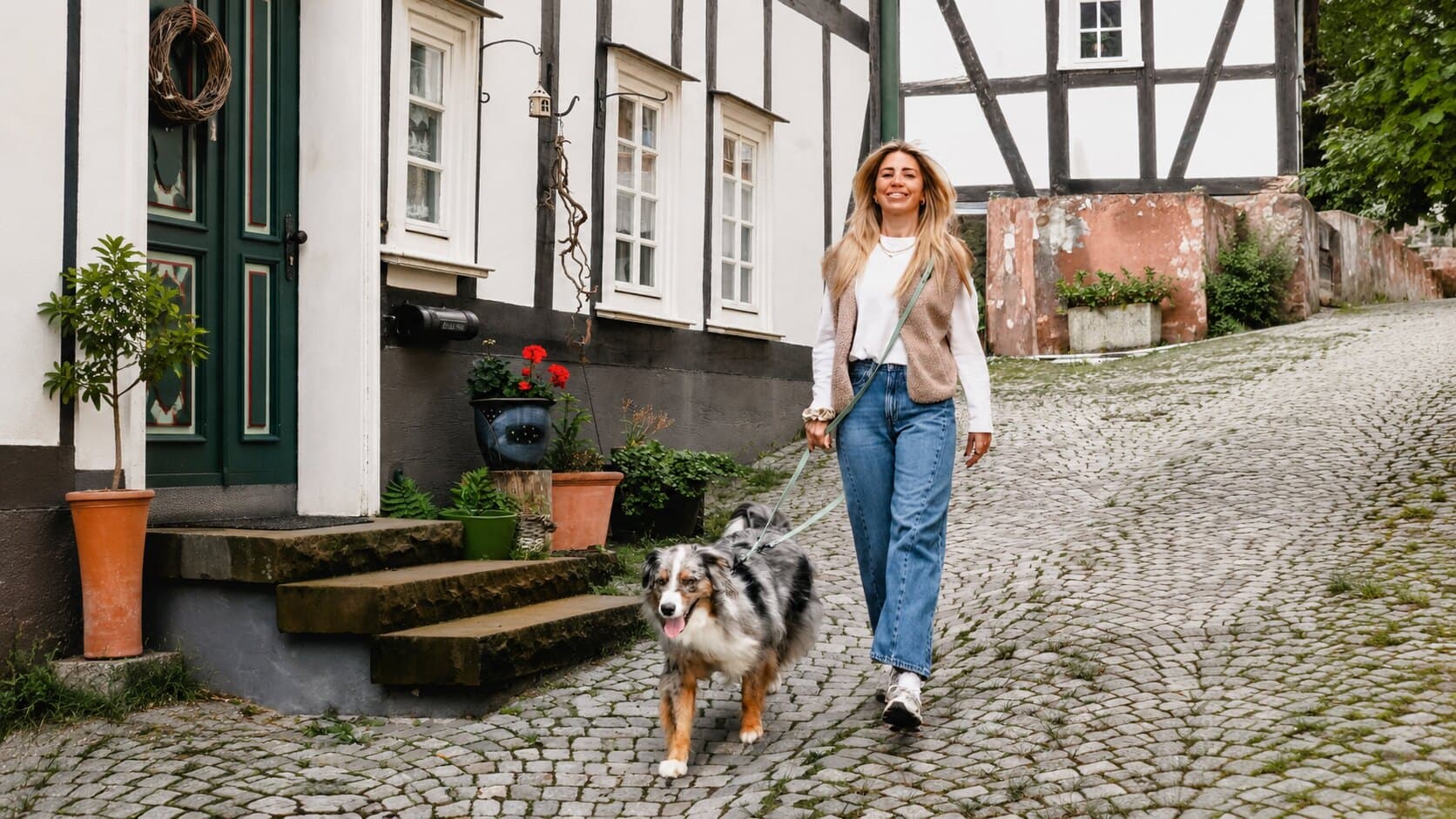 Frau mit Hund an einer langen Leine auf einer Kopfsteinpflasterstraße
