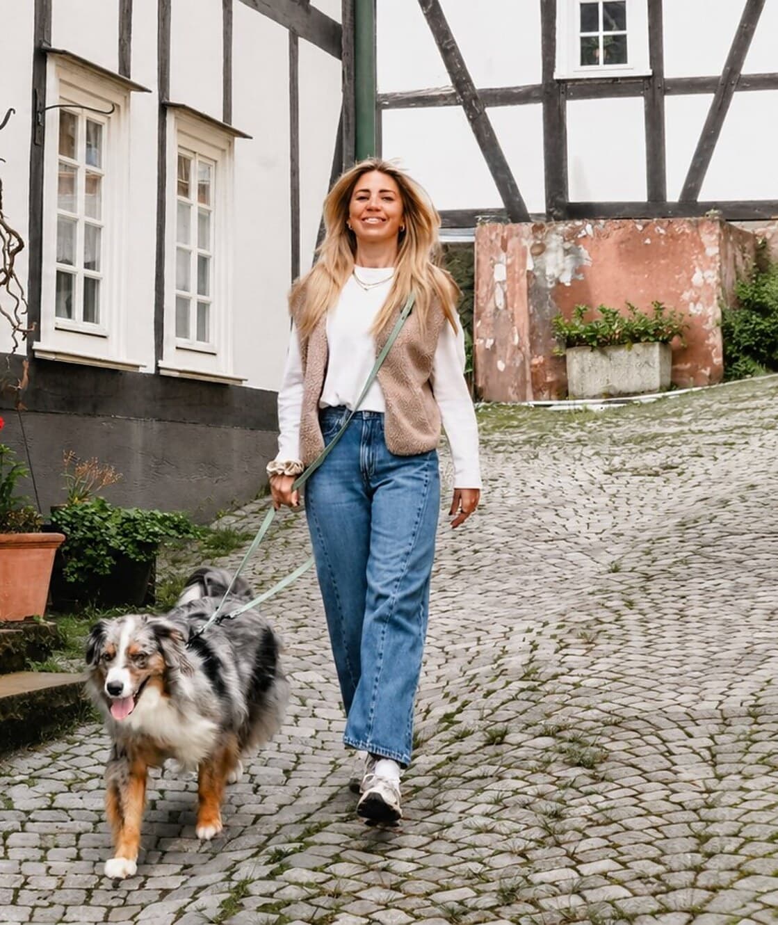 Frau mit Hund an einer langen Leine auf einer Kopfsteinpflasterstraße